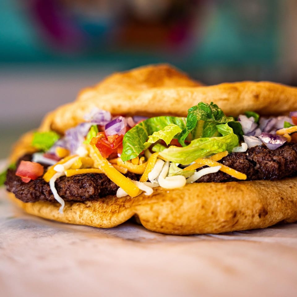 Hope's Frybread taco with ground beef, lettuce, tomatoes, onions, and shredded cheese.