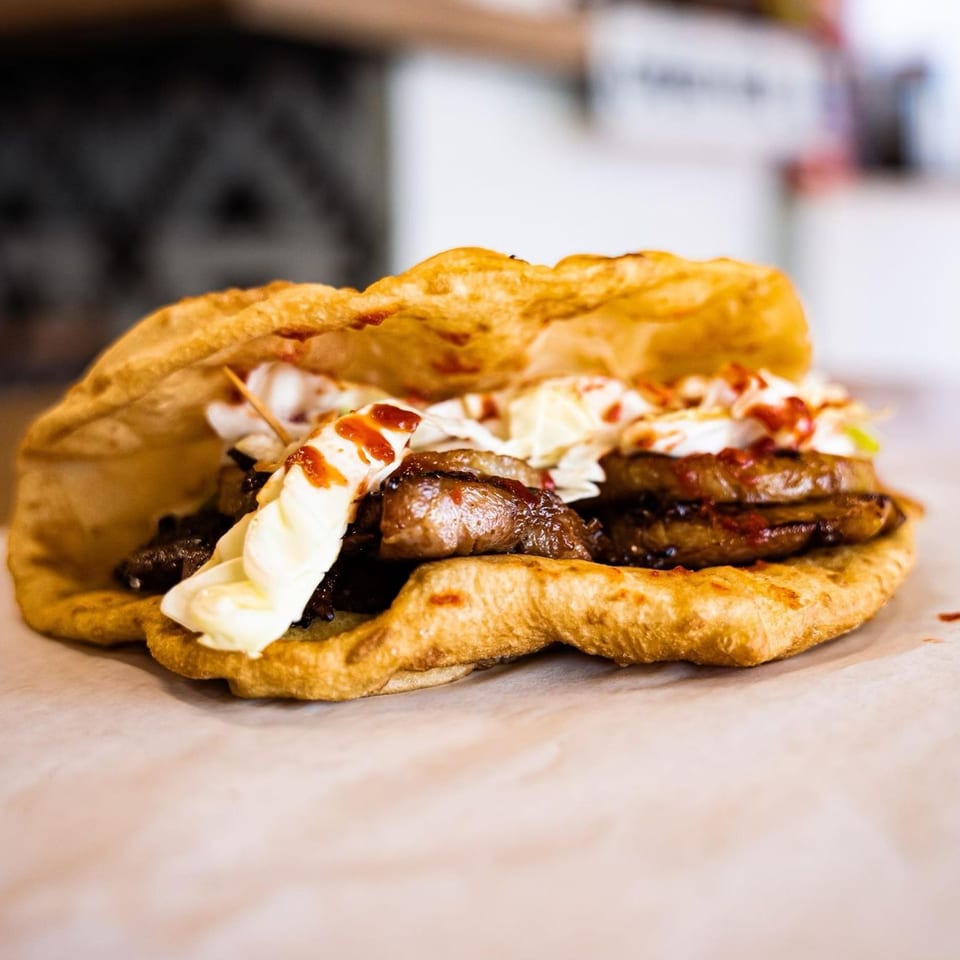 Hope's Frybread with savory filling, white sauce, and red drizzle on parchment paper.