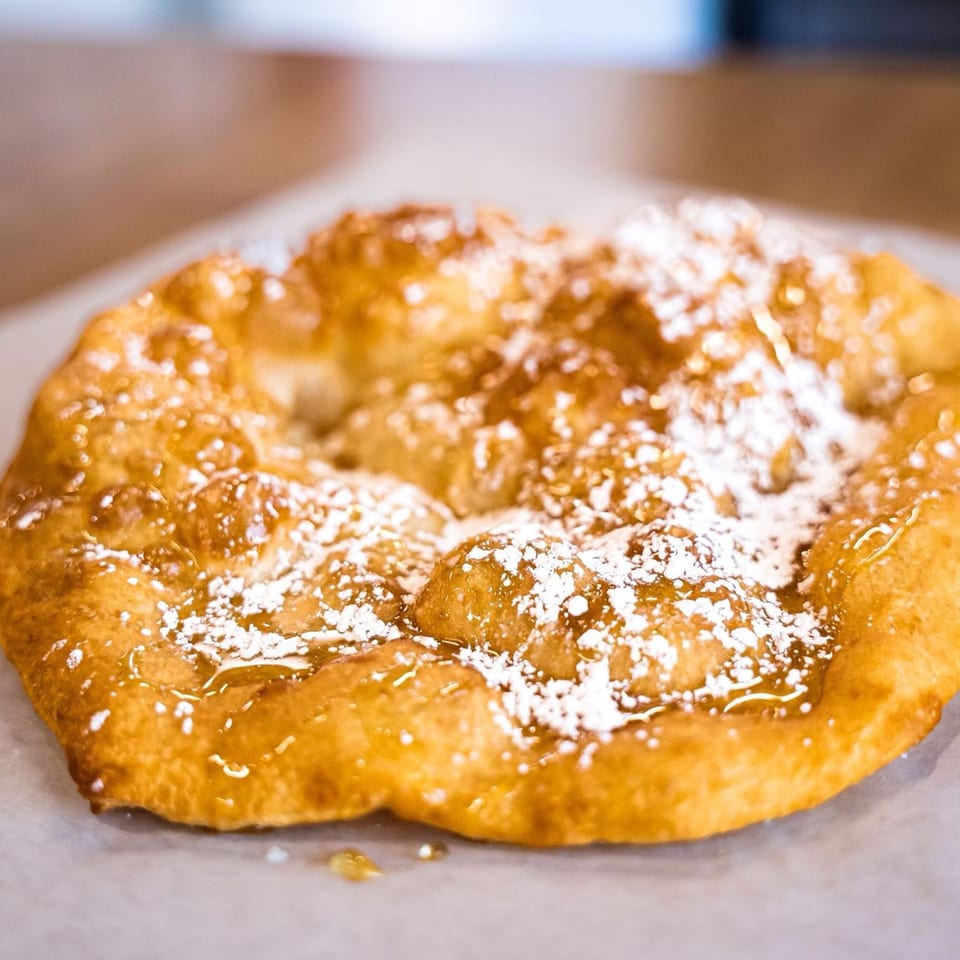 Hope's Frybread, a golden-brown frybread drizzled with honey and powdered sugar.