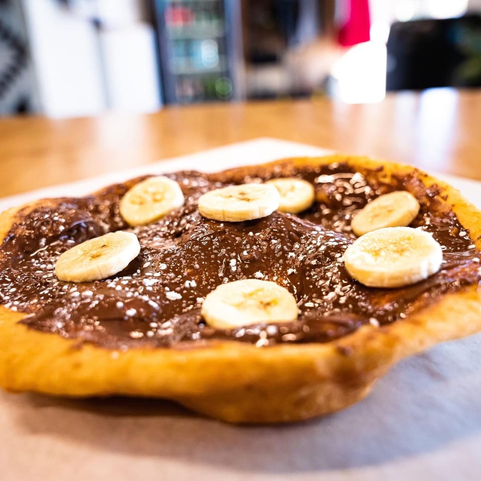 Hope's Frybread dessert with chocolate spread, banana slices, and powdered sugar on a light surface.