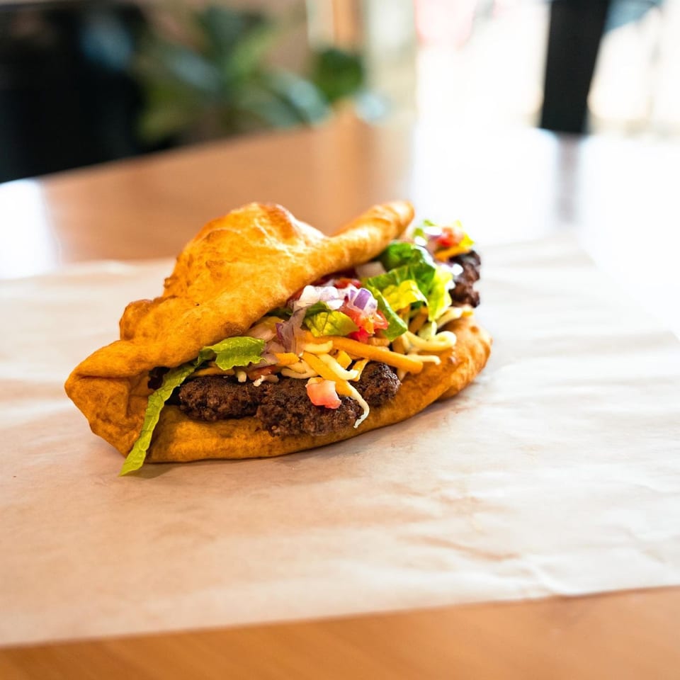 A Hope's Frybread taco with ground beef, lettuce, cheese, and salsa on parchment paper.